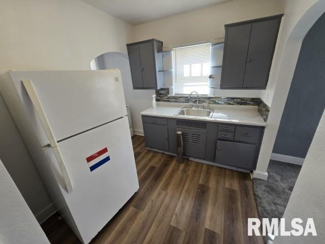 kitchen featuring gray cabinets, a sink, dark wood finished floors, freestanding refrigerator, and arched walkways