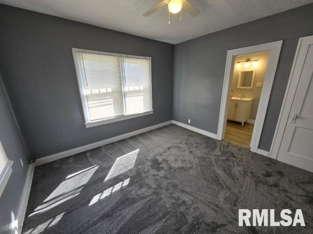 unfurnished bedroom featuring ensuite bath, carpet flooring, baseboards, and a textured ceiling