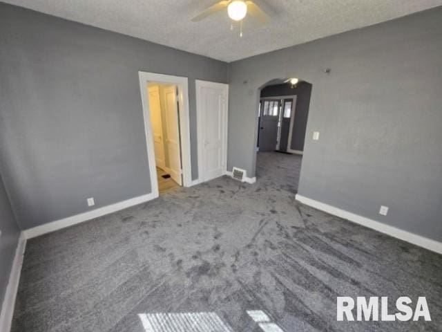 unfurnished bedroom featuring ceiling fan, carpet, baseboards, arched walkways, and a textured ceiling