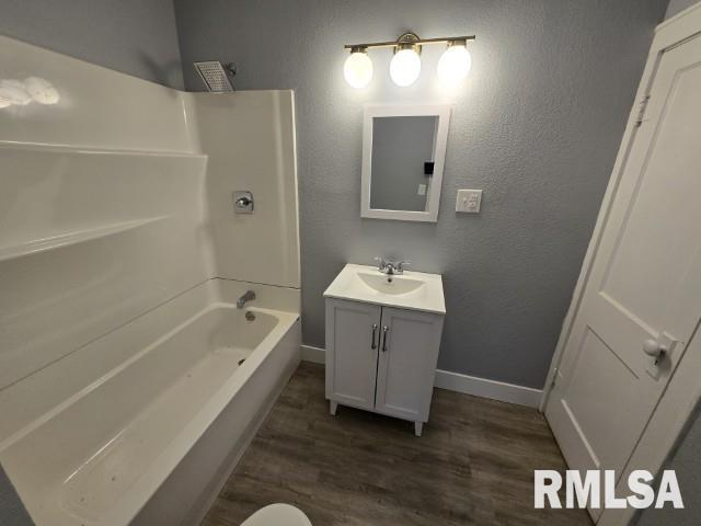 bathroom with vanity, wood finished floors, baseboards, bathtub / shower combination, and a textured wall