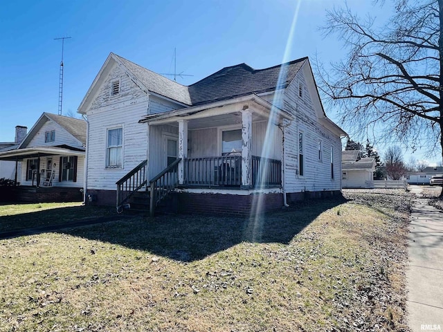 view of front of home with covered porch, a front yard, and a shingled roof