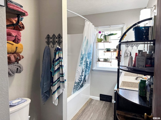 full bath featuring shower / bathtub combination with curtain, wood finished floors, baseboards, a textured ceiling, and toilet