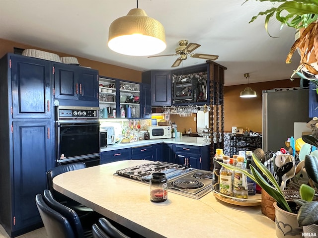 kitchen with oven, blue cabinets, a ceiling fan, light countertops, and hanging light fixtures