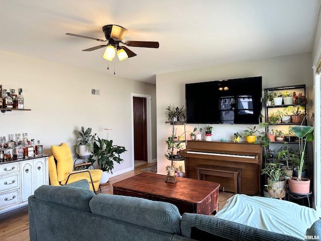 living area featuring a ceiling fan, wood finished floors, visible vents, baseboards, and a dry bar