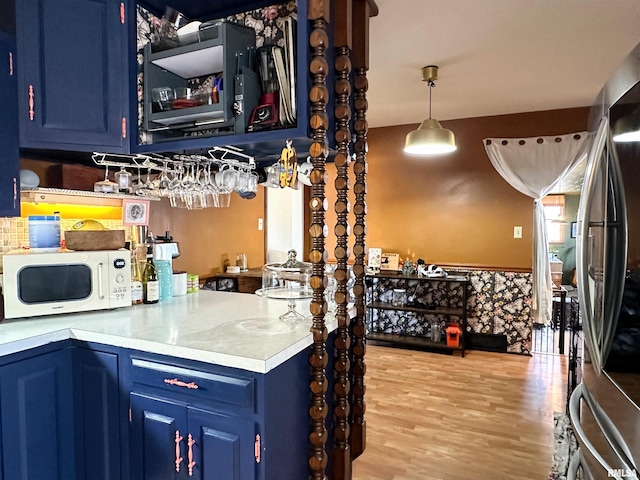 kitchen with light wood-style flooring, blue cabinetry, white microwave, and stainless steel refrigerator