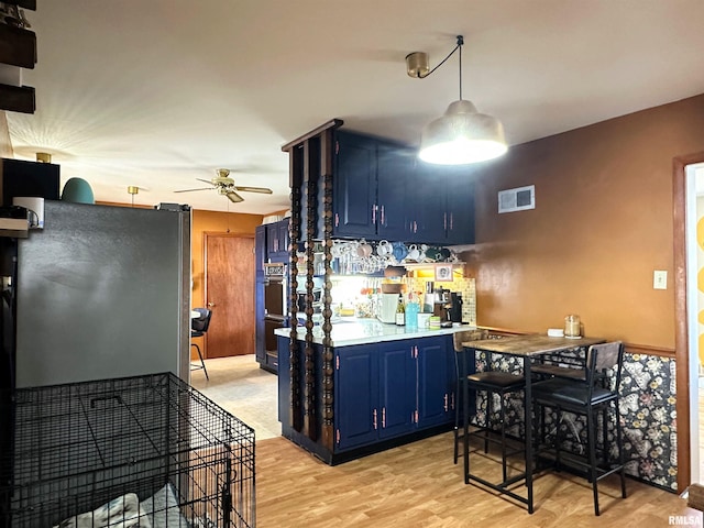 kitchen featuring visible vents, blue cabinetry, ceiling fan, freestanding refrigerator, and light wood-style floors