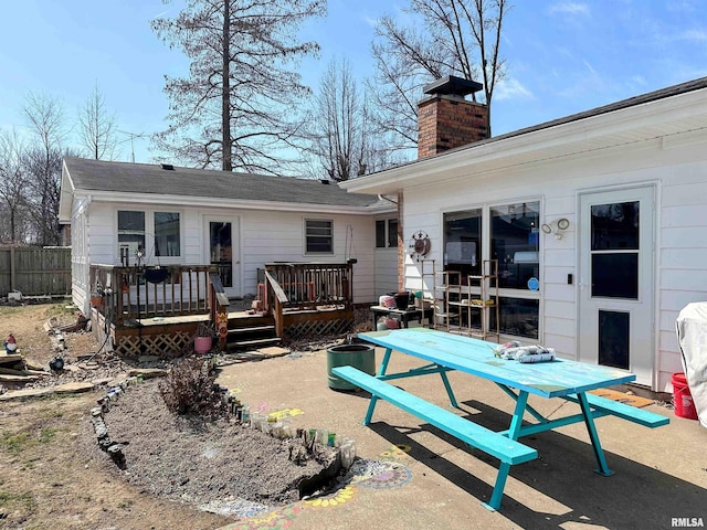 back of house with a patio area, a deck, a chimney, and fence