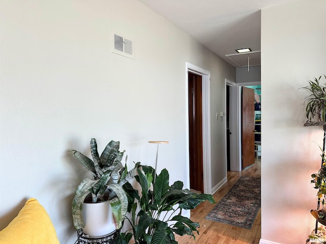 corridor with visible vents, attic access, baseboards, and wood finished floors