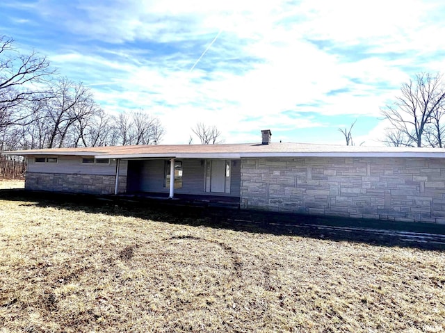 rear view of property with stone siding, a porch, and a chimney