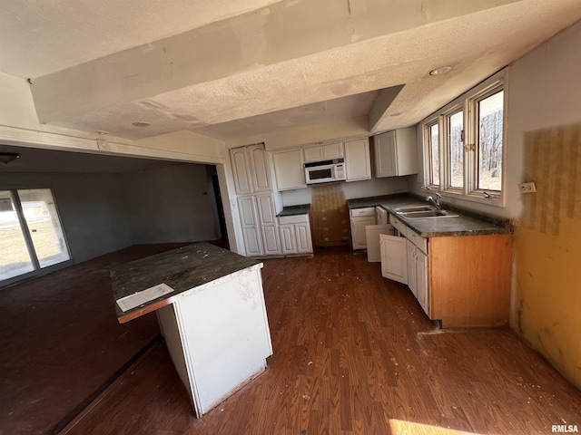 kitchen featuring white microwave, a sink, dark wood-type flooring, a textured ceiling, and dark countertops