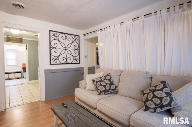 living room featuring wainscoting, wood finished floors, visible vents, and a textured ceiling