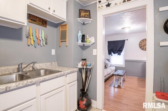 kitchen with a wainscoted wall, open shelves, a sink, light wood-style floors, and white cabinetry