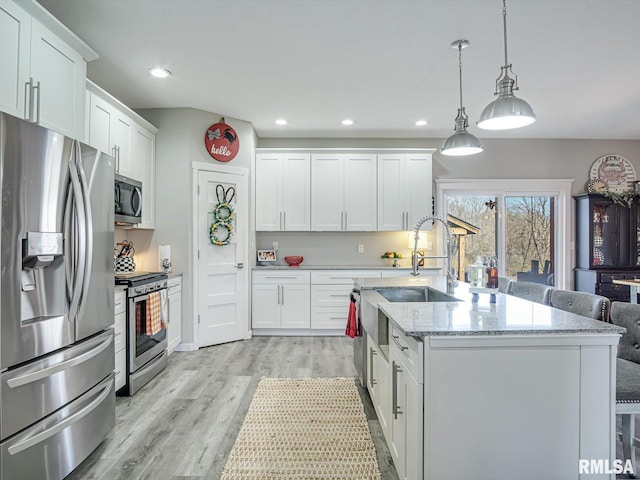 kitchen with an island with sink, a sink, light wood-style floors, appliances with stainless steel finishes, and white cabinetry