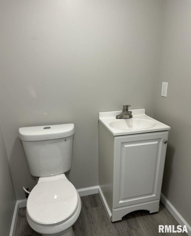 half bath featuring vanity, toilet, wood finished floors, and baseboards
