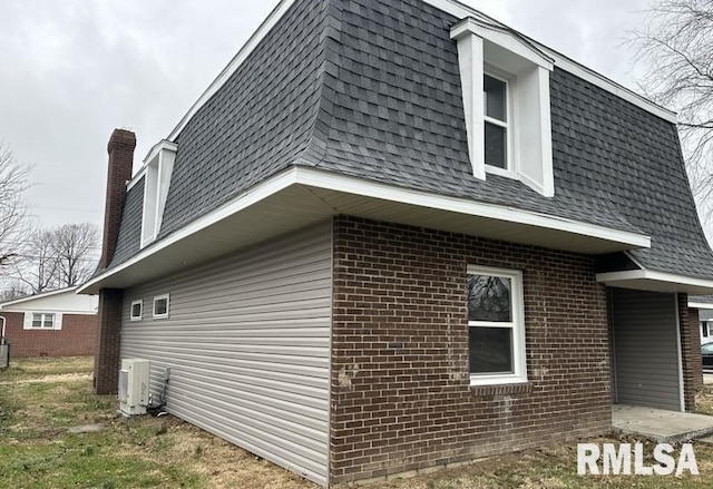 view of side of property with mansard roof, brick siding, and roof with shingles