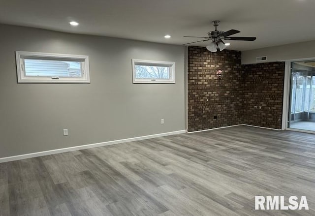 spare room with visible vents, wood finished floors, brick wall, baseboards, and ceiling fan
