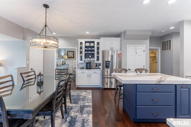 kitchen with a breakfast bar area, white cabinets, high quality fridge, and visible vents