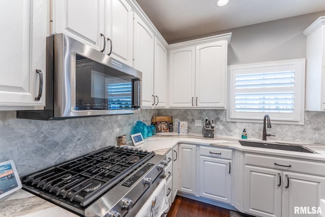 kitchen with light stone counters, decorative backsplash, stainless steel appliances, white cabinetry, and a sink