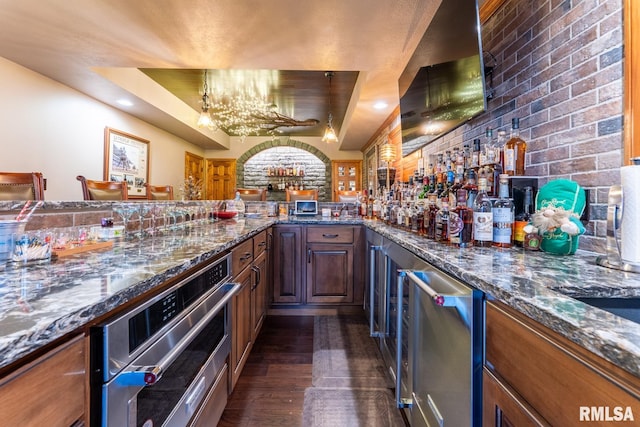 bar with oven, a notable chandelier, dark wood finished floors, brick wall, and bar