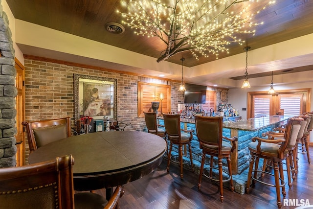 dining space with wood finished floors, brick wall, a tray ceiling, bar area, and wooden ceiling