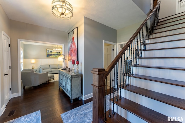 staircase with a notable chandelier, baseboards, visible vents, and wood-type flooring