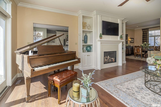 living area featuring ornamental molding, ceiling fan with notable chandelier, wood finished floors, a fireplace, and baseboards