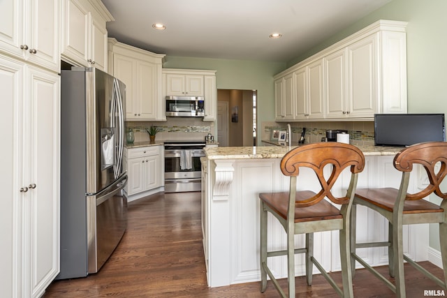 kitchen featuring backsplash, light stone countertops, dark wood finished floors, appliances with stainless steel finishes, and a peninsula