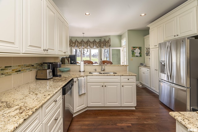kitchen featuring dark wood-type flooring, a sink, tasteful backsplash, stainless steel appliances, and a peninsula
