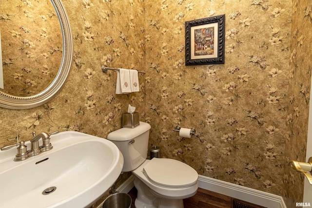 half bath featuring toilet, wood finished floors, baseboards, and a sink