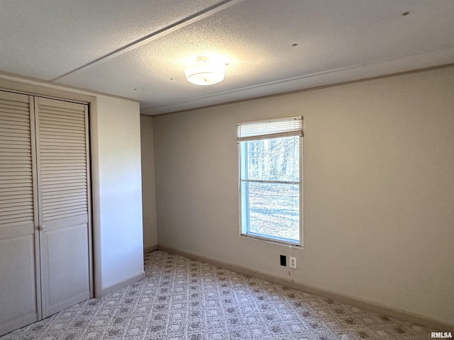 unfurnished bedroom with light colored carpet, baseboards, a closet, and a textured ceiling