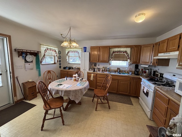 kitchen featuring under cabinet range hood, light floors, white gas range, brown cabinets, and a sink