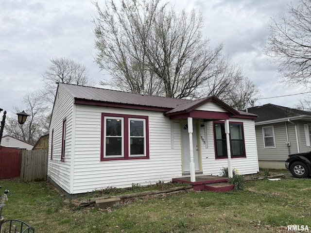 bungalow with a front lawn, fence, and metal roof