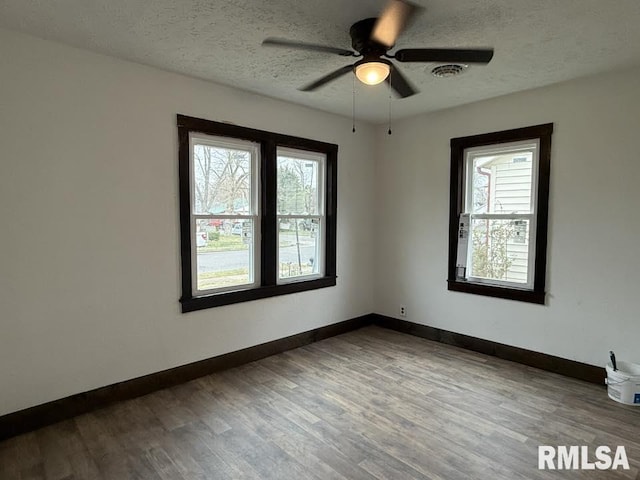 unfurnished room featuring visible vents, a textured ceiling, baseboards, and wood finished floors