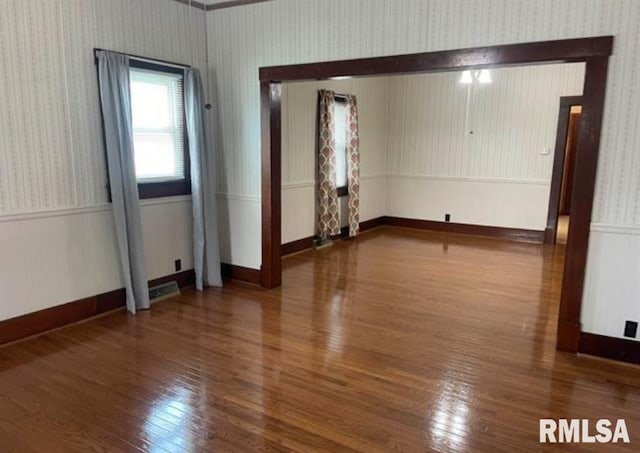 spare room with hardwood / wood-style floors, visible vents, wallpapered walls, and wainscoting