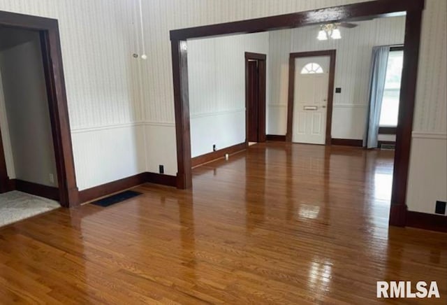 foyer entrance featuring a wainscoted wall, wallpapered walls, and wood finished floors