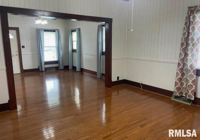 unfurnished room with baseboards, a wainscoted wall, wood finished floors, and wallpapered walls