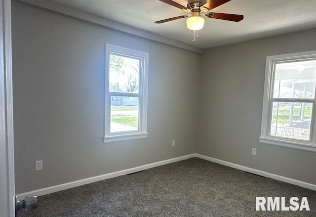 empty room featuring baseboards, a wealth of natural light, and dark colored carpet