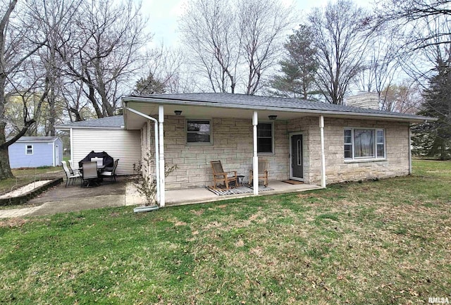 rear view of house featuring stone siding, an outdoor structure, a lawn, and a patio