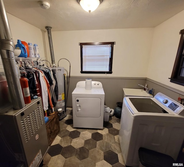 laundry area with water heater, washing machine and clothes dryer, a sink, laundry area, and wainscoting