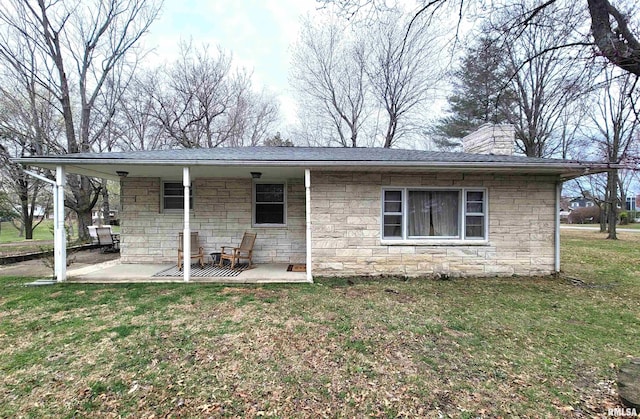 rear view of house featuring stone siding, a chimney, a patio, and a yard