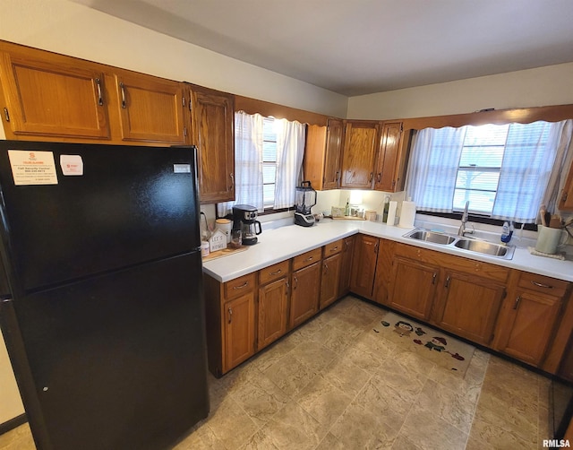 kitchen featuring light countertops, a sink, freestanding refrigerator, brown cabinetry, and plenty of natural light