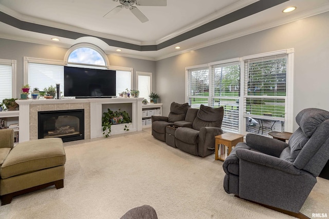carpeted living area featuring crown molding, a tray ceiling, a ceiling fan, recessed lighting, and a tile fireplace