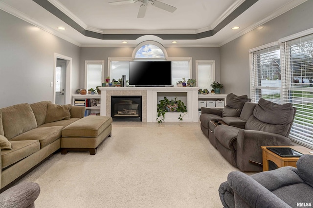 living room with a raised ceiling, crown molding, light colored carpet, and ceiling fan