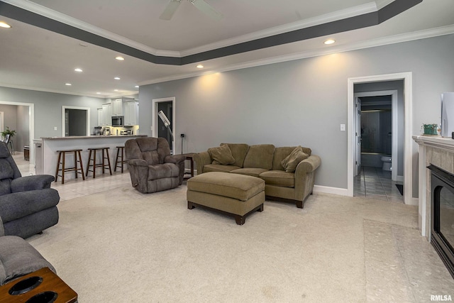 living area with a raised ceiling, a tiled fireplace, crown molding, recessed lighting, and light carpet