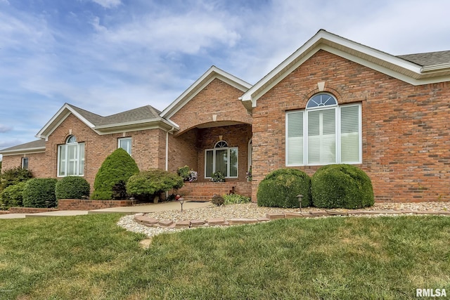 view of front facade featuring roof with shingles, brick siding, and a front lawn