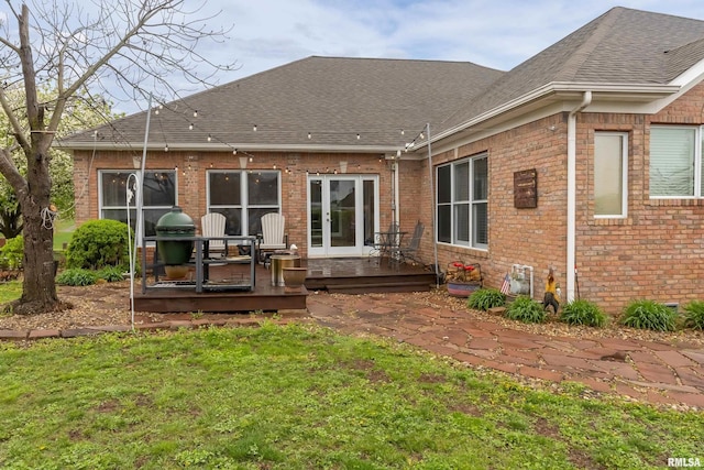 rear view of house featuring roof with shingles, a yard, brick siding, and a wooden deck