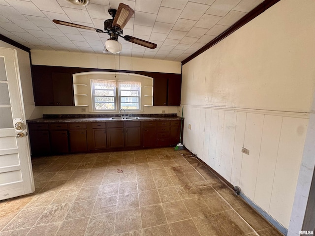 kitchen featuring open shelves, a sink, ceiling fan, dark countertops, and wainscoting