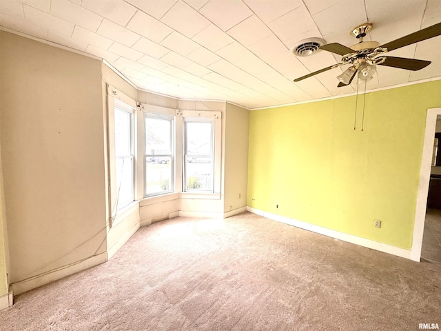 carpeted spare room featuring crown molding, baseboards, a ceiling fan, and visible vents