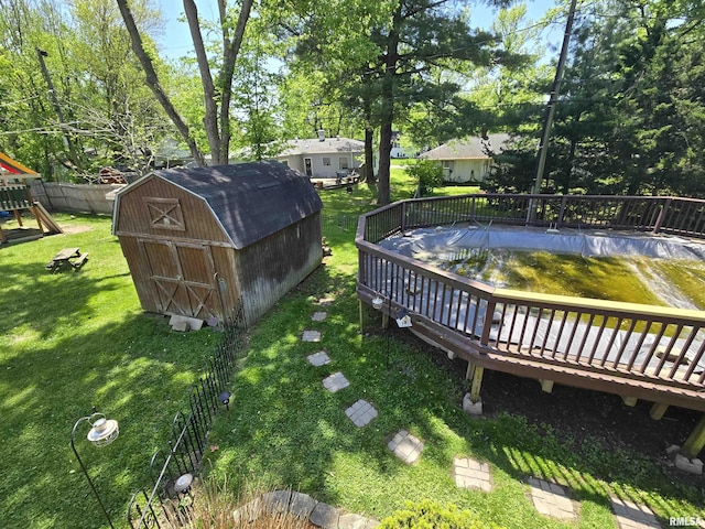 view of yard with a wooden deck, an outdoor structure, a storage shed, a playground, and fence