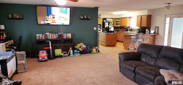 living area featuring ceiling fan, light carpet, and a healthy amount of sunlight